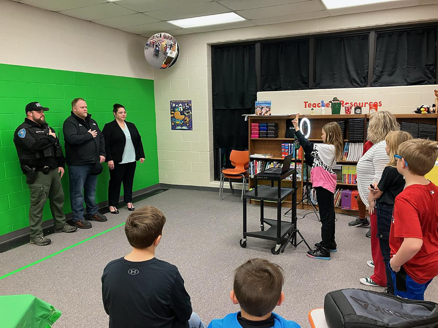 Truesdale Police Chief Casey Doyle, Mayor Chris Watson, and City Clerk Elsa Smith Smith-Fernandez prepare to lead students in the Pledge of Allegiance as part of Rebecca Boone Elementary's daily news videos produced by students.