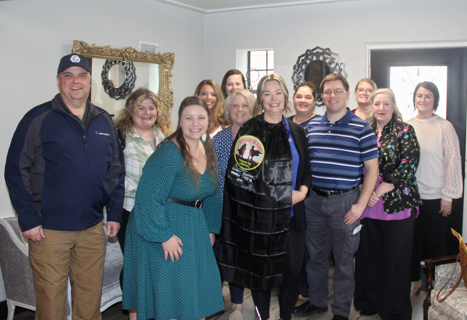 HIDDEN HERO — Stacey Blondin receives her very own superhero cape as she is joined by staff members at Main Street real estate, along with community supporters of the Hidden Heroes program.