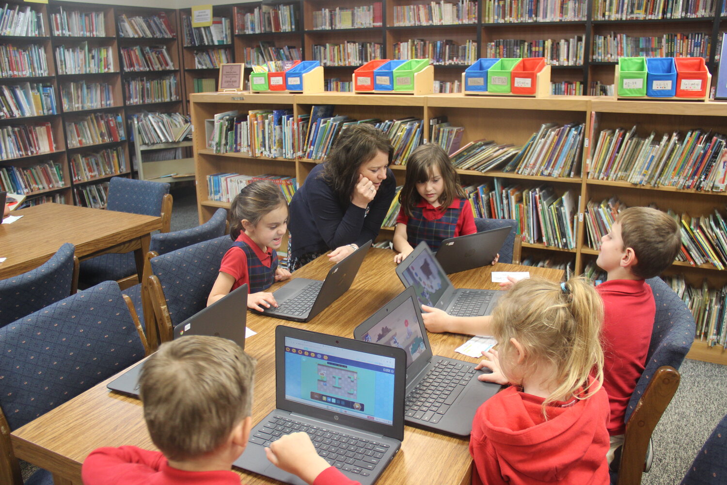 Holy Rosary Principal Lori Racine works with Elizabeth Weisler and Delilah Bennett during technology class in the school’s library on May 15.