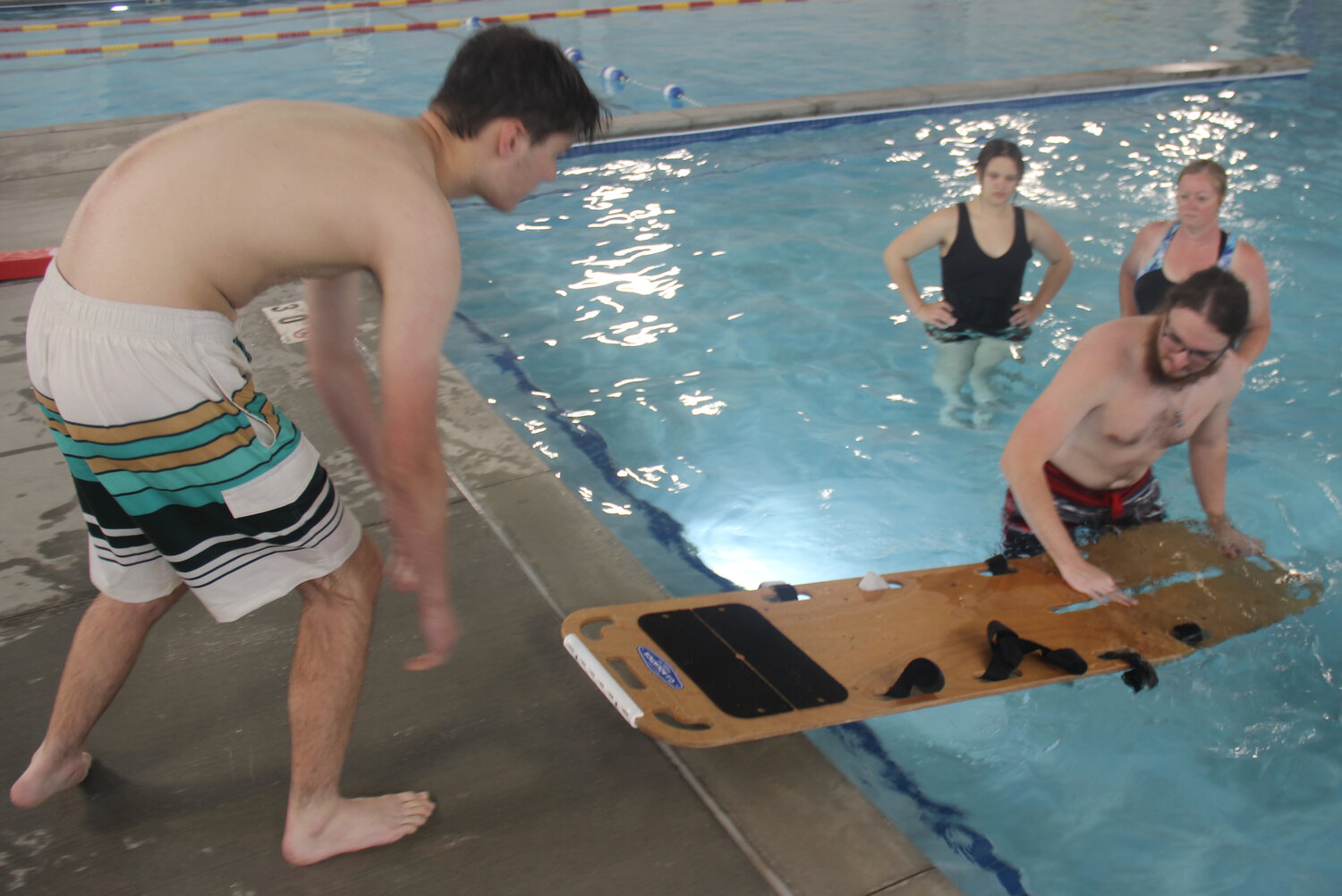 Jacob Nagel works with Cole McBride to handle the backboard during lifeguard training while Miakoda Rhodes and Tamara Wurth look on.