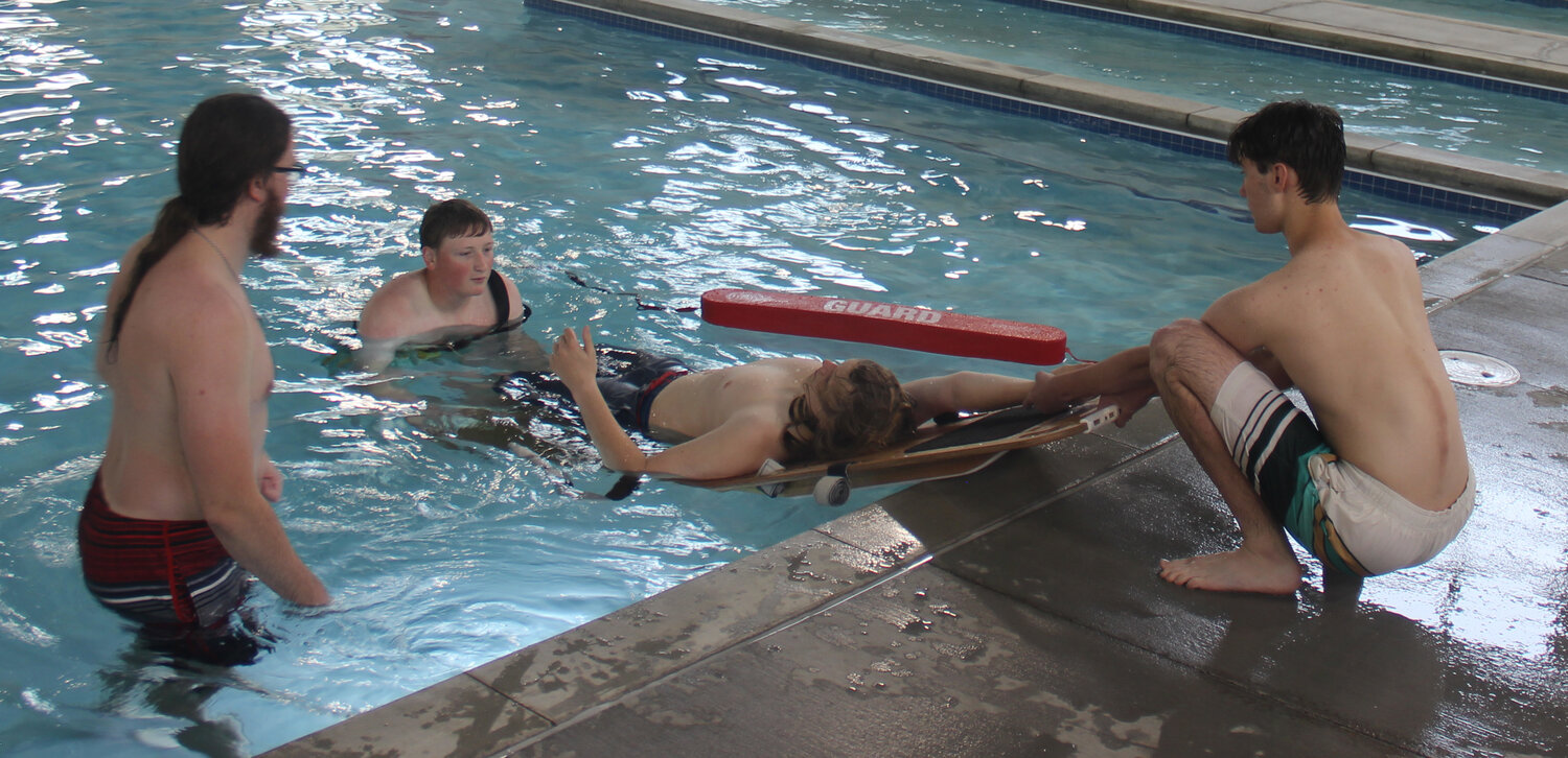 Cole McBride offers instruction and encouragement to Cooper Stone, in the water, and Jacob Nagel, on land, as they team up to "rescue" fellow lifeguard candidate Hunter Grube during an exercise on May 19.
