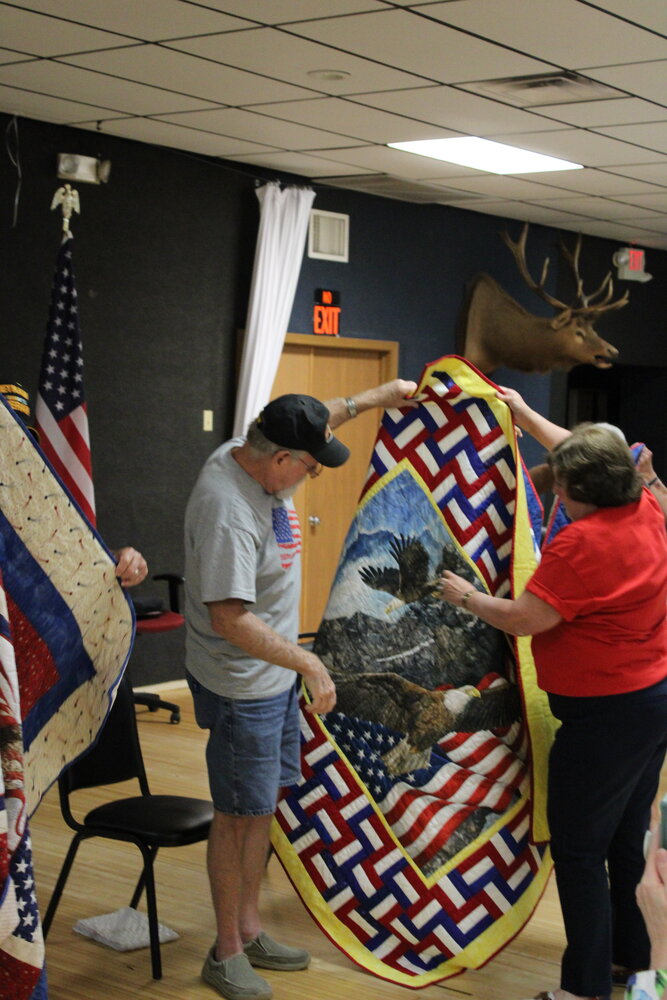 Marlene Walton, right, helps Rob Miller unfold and display the quilt he was presented in honor of his service in the U.S. Army.