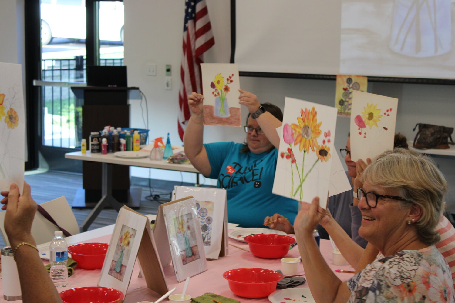 Hillary Edwards, Jaime Strauss, and Lisa Owenby hold up their partially finished paintings to show off their work to the rest of the watercolor painting group.