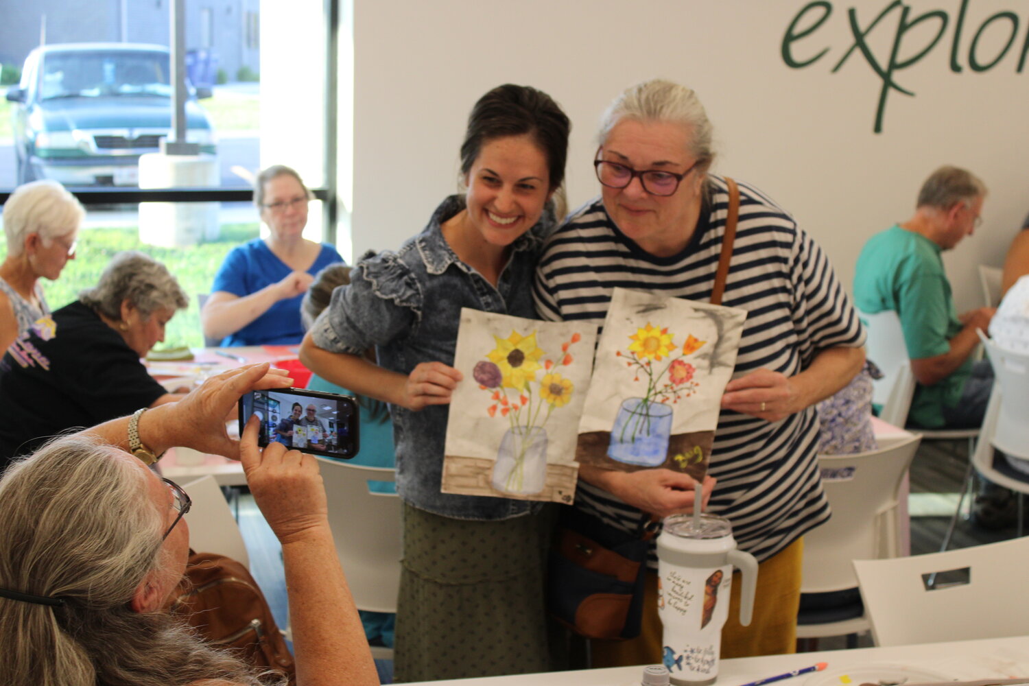 Shannon Gardner and Brigitte Gardner pose with their completed watercolor designs while Nancy Amburgey takes their picture at the end of the watercolor event.