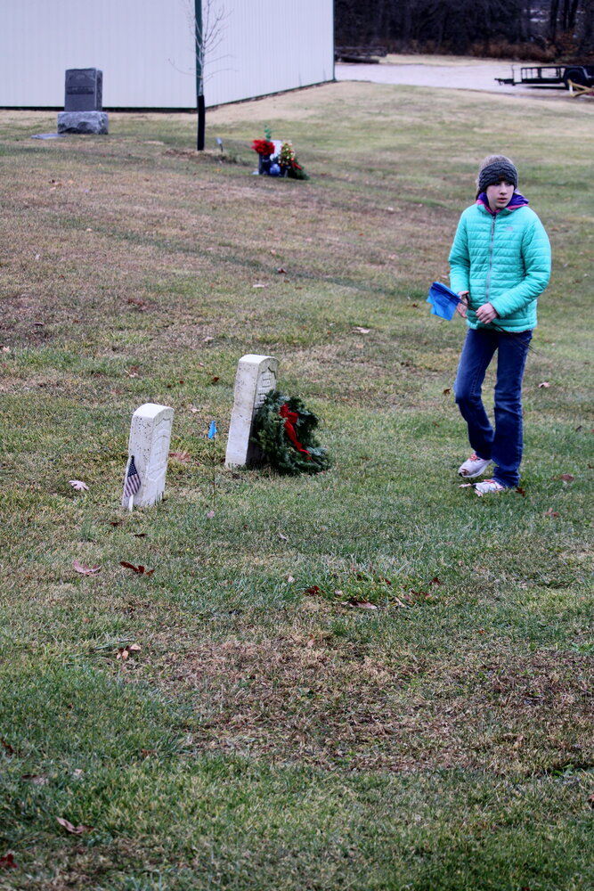 A volunteer lays a wreath on the headstone of a veteran's grave at the Warrenton City Cemetery.