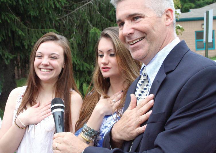 HONORARY CITIZEN: Erin Clarke (far left) of Australia lead the school in the Pledge of Allegiance. She is pictured with Hoxsie Principal Gary McCoombs and his daughter, Kayla. Erin and Kayla became friends while attending a school in Vienna, Austria.