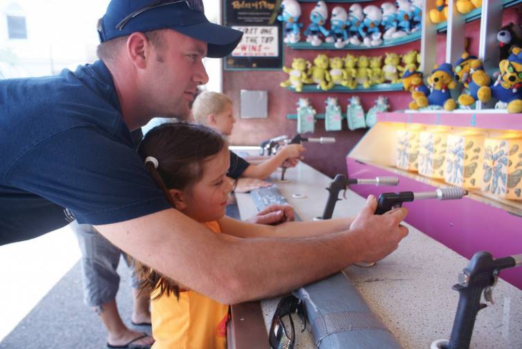 TAKING AIM: Tom Campbell helps his 6-year-old daughter Samantha take aim for a prize in the squirt gun carnival game. With the help of her father, she won a stuffed animal prize.