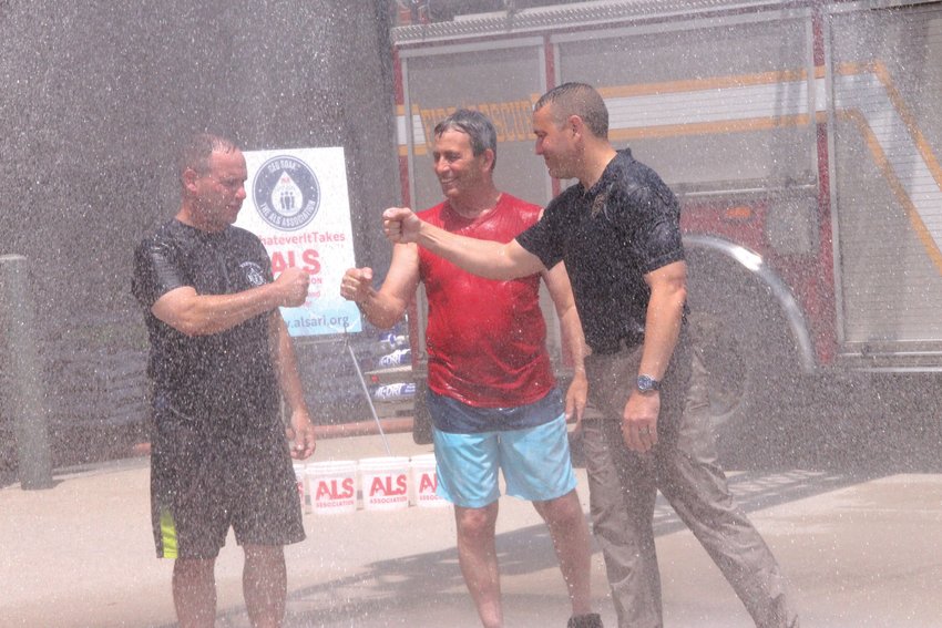 NOT WET ENOUGH: Mayor Picozzi, Fire Chief McMichael, and Police Chief Connor decided the rainy summer hadn&rsquo;t soaked the state enough, and got drenched on Tuesday for ALS research. Here they bump fists under a shower provided from a ladder truck in front of Station 1 in Apponaug Tuesday.