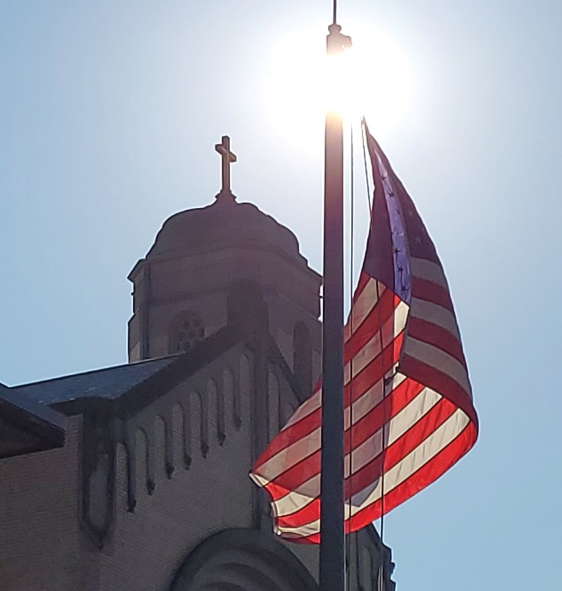 LOOMING SYMBOLS: The American flag flapped high above the crowd gathered outside St. Rocco School for last Friday&rsquo;s &ldquo;Prayer for Peace and Healing on the 20th Anniversary of 9/11.&rdquo;