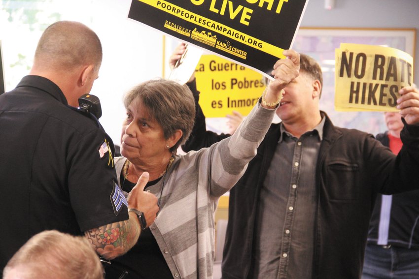 DEFIANT: A protestor continues to voice her opinion although a police officer stands ready to eject her from the meeting. (Cranston Herald photos)