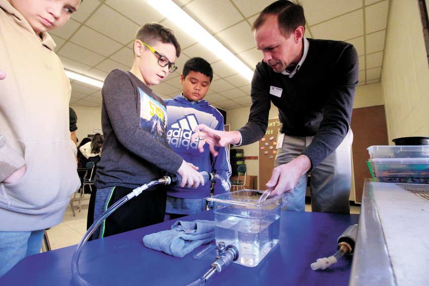 IT FLOWED: Cody Morin looks on as his Hoxsie fourth grade classmate Mason Kue, assisted by Ross McLendon of the international software engineering company DS with offices in Johnston compresses a hand pump to illustrate how the human heart chamber and value system functions. (Warwick Beacon photos by John Howell)