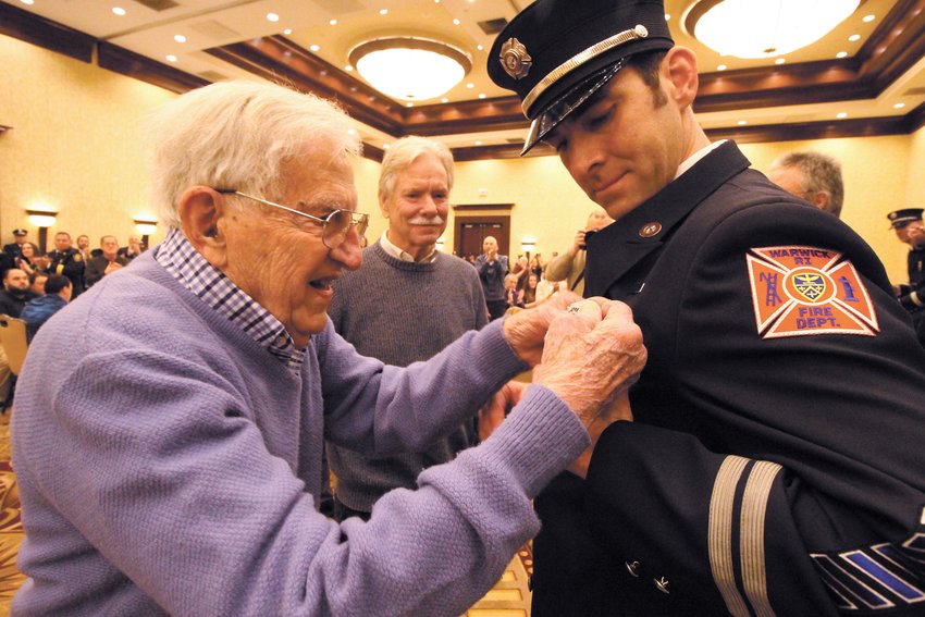 Their service applauded: More than 300 people stood to applaud when WWII veteran Maurice Roland Boulais participated in  the promotional ceremony of 21 firefighters Wednesday night at the Crowne Plaza. Boulais with his son-in law Henry Andrews standing by affixed the badge of Assistant Fire Marshal Ethan Andrews, Henry&rsquo;s son. (Warwick Beacon photos)