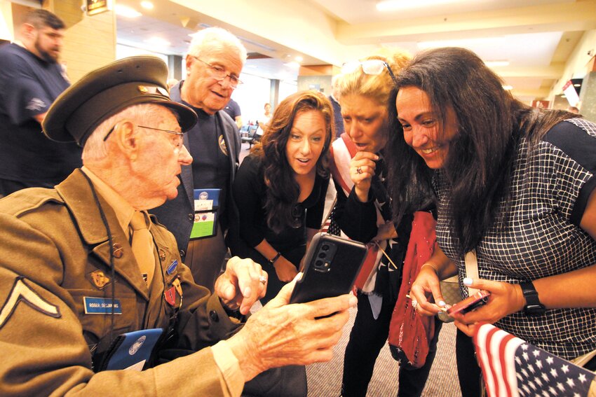 98 AND HIGH TECH: WWII Army veteran Roger Desjardins of North Providence, the oldest member of Honor Flight Freedom that left from Green Airport Monday, pulled out his cell phone to accompany stories he was recounting. Behind him is North Providence Mayor Charles Lombardi who was Desjardins&rsquo; guardian for the flight. (Cranston Herald photos by John Howell)