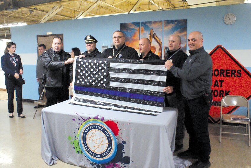 ON BEHALF OF THE SCHOOL: Major Todd Patalo, and Chief of Police Colonel Michael Winquist stand with School Resource Officers Randy Babcock, John Rocchio, Matthew Davis, and Rob Arruda while they hold a flag signed by the Apprenticeship Exploration School’s students and staff. (Photos by Steve Popiel)