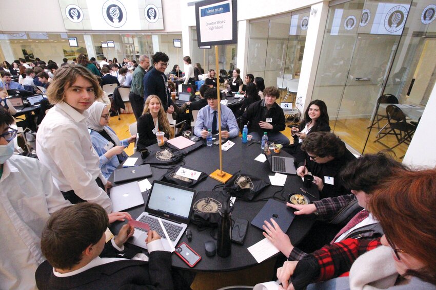 TEAM TABLE: Cranston West RI Academic Decathlon coach Christine Luther-Morris, bottom right, and  the team before the 2023 competition at Bryant University. Teams from 15 schools involving nearly 200 students will compete this Sunday in the event being hosted again by Bryant. (Cranston Herald photos)