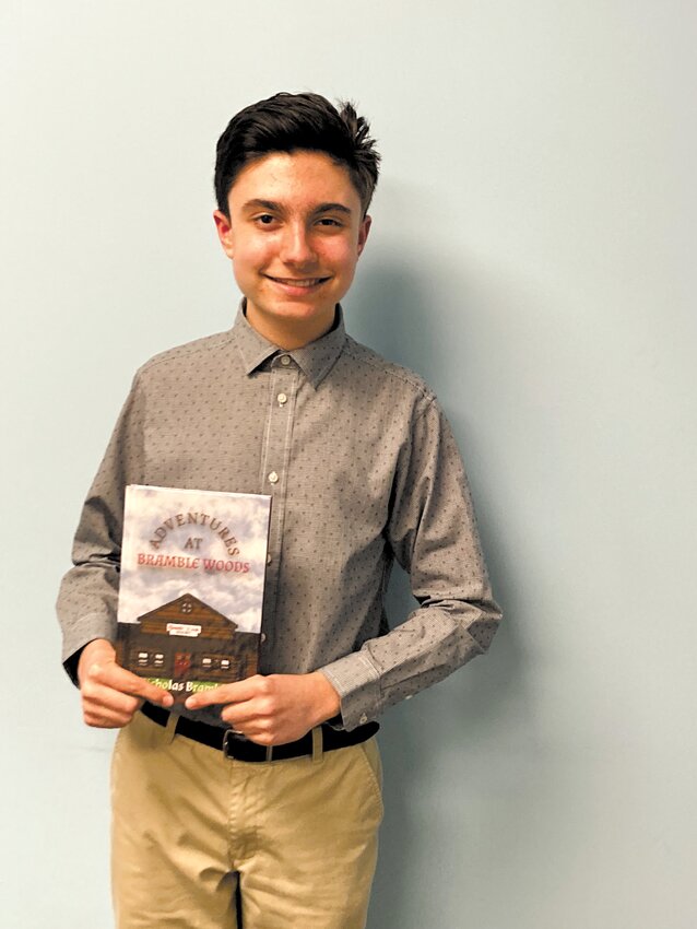 IMAGINATION ON PAPER: Nicholas Bramble poses with his book Adventures at Bramble Woods, which he recently published after two years of writing.