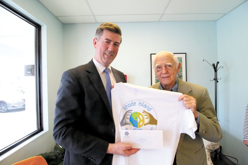 MAKING A WORLD OF DIFFERENCE: Warwick Senator Matthew LaMountain, sponsor of a $5,000 Senate legislative grant is joined by John Howell, president of the Rhode Island Academic Decathlon at a recent presentation. They are holding the T-shirt of this year’s decathlon with the theme “humanity and technology.”  The shirt designed by Liam Harnois was one of many created by students of the graphics arts department at the Warwick Area Career and Technical Center.  (Warwick Beacon photo)