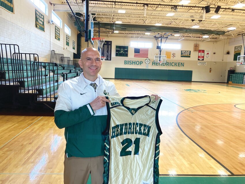 A PROUD COACH: Bishop Hendricken head basketball coach Jamal Gomes holds up Joe Mazzulla’s jersey in the gym where Mazzulla spent his high school days playing.