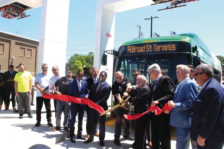 RIPTA&rsquo;S RED RIBBON: With some help wielding giant shears, Senator Jack Reed cuts a ceremonial ribbon in front of an R-Line electric bus, accompanied by RI politicians and RIPTA officials.