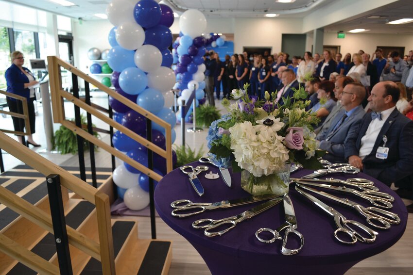 GATHERED TO CELEBRATE: The hospital&rsquo;s Director of Business Development, Joy Helgerson, introduced the crowd to the ribbon-cutting celebration speakers last Thursday. A pile of scissors awaited a group of public and private officials, who ceremoniously cut the ribbon after a short speaking program on July 25.